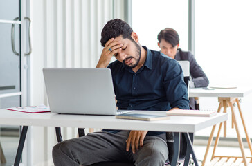 Indian stressed depressed exhausted bearded male businessman sitting at workstation with laptop...