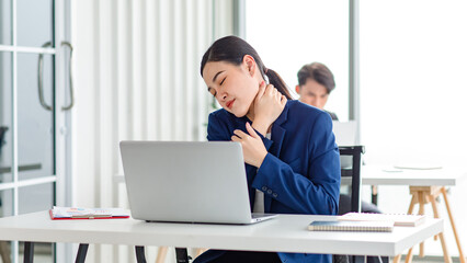 Fototapeta na wymiar Asian stressed exhausted tired female businesswoman secretary working late and hard sitting at workplace in company take off glasses hold hand massaging painful shoulder from office syndrome symptom
