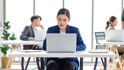 Closeup shot of millennial Asian young beautiful smart professional female businesswoman employee in formal suit sitting working on workstation desk typing laptop notebook computer in company office