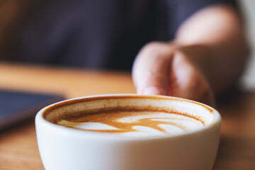 Closeup image of a woman holding and drinking hot coffee while working on laptop computer