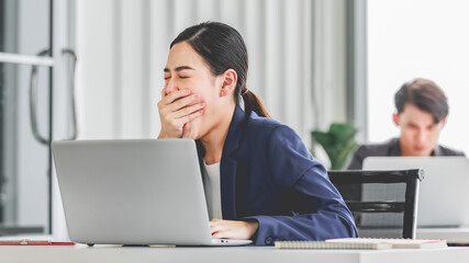 Closeup shot of millennial Asian young stressed depressed sleepy female businesswoman employee sitting holding hand on messy hair working on workstation desk via laptop notebook computer in office