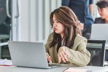 Closeup shot of millennial Asian young stressed depressed sleepy female businesswoman employee sitting holding hand on messy hair working on workstation desk via laptop notebook computer in office