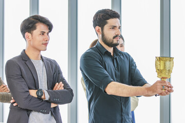 Millennial Asian young smart happy proud cheerful professional successful male businessman in casual suit standing smiling holding gold trophy prize celebrating top talent sales staff employee award