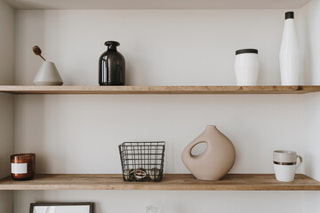 Decorated shelf on white wall. Aesthetic luxury minimalist home interior design decoration. Elegant Scandinavian, hygge style interior. Picture frames, fragrance, vase, books, candle