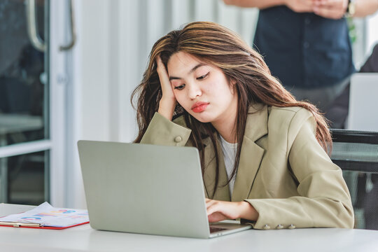Closeup shot of millennial Asian young stressed depressed sleepy female businesswoman employee sitting holding hand on messy hair working on workstation desk via laptop notebook computer in office