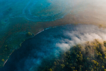 Naklejka na ściany i meble Aerial view of a beautiful summer landscape with a fog while dawn. Photo from drone of a foggy landscape in spring. Top view to land while sunrise. Early morning in nature, misty weather.