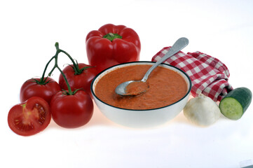 Assiette de gaspacho maison avec une cuillère et ses ingrédients sur fond blanc