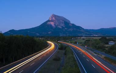 Car lights driving on the road at dusk with the mountains in the background.