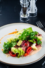 Fresh salads with beef steak, green leaves, arugula and sweet sauce on dark background