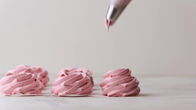 Squeezing whipped pink cream with pastry bag  for raspberry marshmallow. Close up of confectioner making marshmallow on the white background