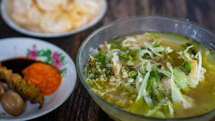 Soto Kudus is Indonesian food delicacy, chicken soup with blur background of Indonesian crackers (krupuk)
