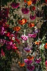 Italian decor with flowers hanging from ribbons: orange and pink chrysanthemums, roses, allium. Floral arrangements in the background.
