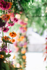 Italian decor with flowers hanging from ribbons: orange and pink chrysanthemums, roses, allium. Floral arrangements in the background.