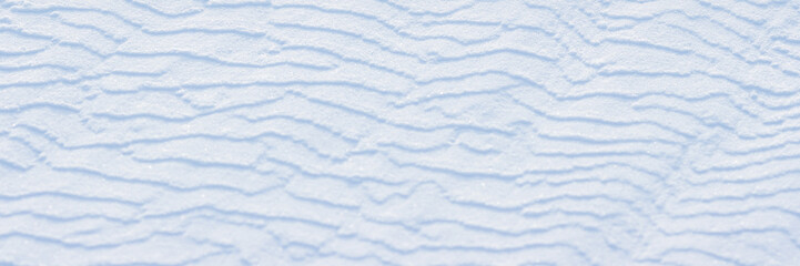 Beautiful winter background with snowy ground. Natural snow texture. Wind sculpted patterns on snow surface. Wide panoramic texture for background and design.