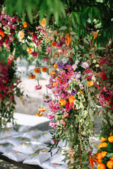 An arch entwined with multi-colored bright flowers and vines in an Italian garden. In the background is a bench with many pillows.
