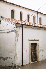 An old white dilapidated house on a European street with a diluted wooden door and arched windows.