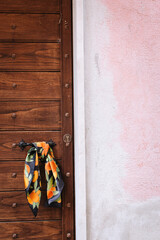 Women's silk scarf with tangerines is tied to the handle of a wooden door. To the right of the door is a pink wall.