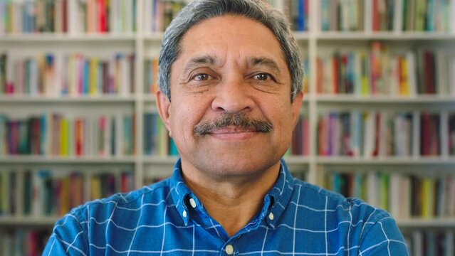 Portrait of an Indian man in a library. Elderly professor or teacher with moustache is pleased with the research he has done in front of a book shelf. Learning and education in the senior years.
