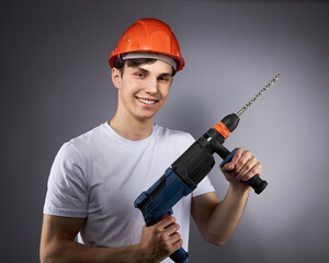 a young construction worker in a hard hat and a white T-shirt with a puncher in his hand.