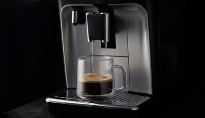 Freshly brewed coffee is poured from the coffee machine into glass cups.