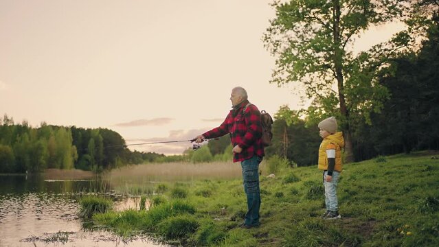 grandpa and little boy are fishing on coast of picturesque pond in woodland, family weekend