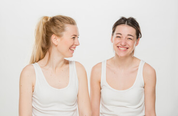 two girls are laughing.close-up portrait of two girls in white t-shirts on a white background isolated. two young Ukrainian girls, a brunette and a blonde, laugh merrily.