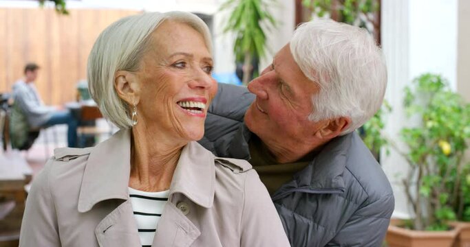 Loving senior couple showing affection and love at a restaurant. Retired husband kissing his wife while celebrating their anniversary together. Mature man and woman showing appreciation and care