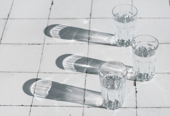glass with clean clear water and sharp shadows stands on a white wood table. top view of glass with water on white tableon a tiled table