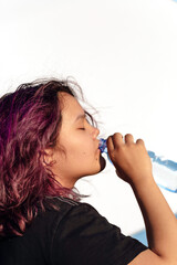 Asian girl with purple drinks water from a plastic bottle on a white isolated background. Generation Z. The concept of thirst