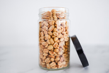 glass jar of peanuts on white marble background, healthy pantry ingredients