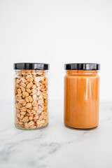 glass jars with peanuts and peanut butter on white marble background, healthy pantry ingredients