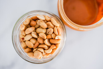 glass jars with peanuts and peanut butter on white marble background, healthy pantry ingredients