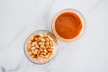 glass jars with peanuts and peanut butter on white marble background, healthy pantry ingredients