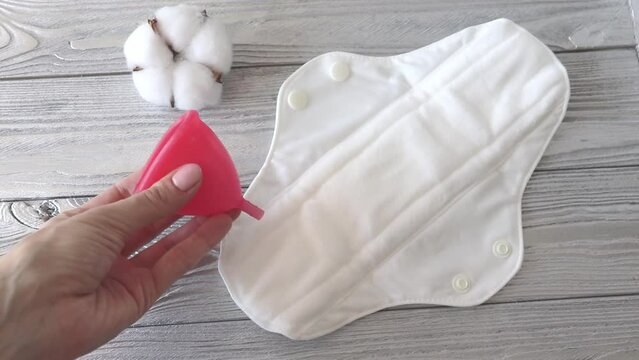 A reusable pad and menstrual cup in a woman's hands. Zero waste, stop plastic.