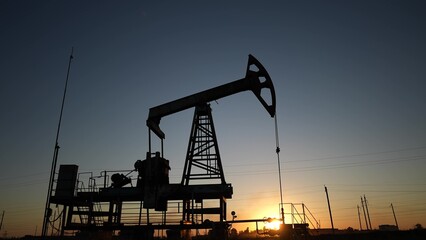oil production. silhouette oil and gas production rig at sunset glare. oilfield business a...