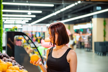 Young woman choosing oranges while shopping in supermarket.