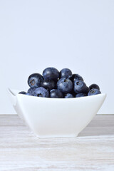 Blueberries in porcelain bowl, light background and copy space.