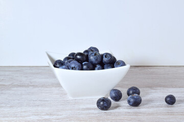 Blueberries in porcelain bowl and scattered on the table.