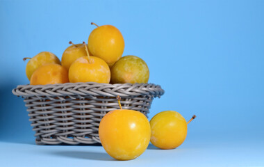 Fruit, yellow plum and in wicker basket. Blue background and copy space.