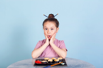 Cute smiling little girl with with sushi on red background. Student child girl eating sushi and rolls - commercial concept