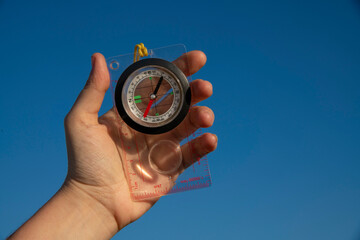 Hand holding compass on the blue sky background.