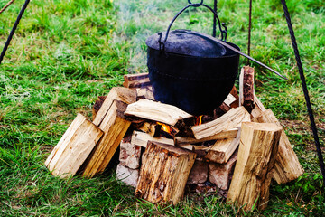 An old round cauldron hangs over the fire and firewood. Cooking food of ancient peoples in the...
