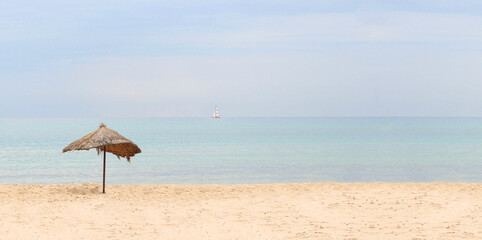 Banner of the seascape. Straw beach umbrella on a tropical sandy beach on a background of blue sea on a sunny day. Idyllic travel and summer vacation concept