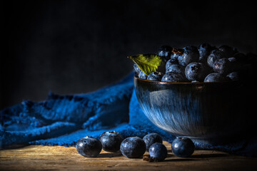 Blueberries in a blue bowl with napkin on wooden board table and background - dark and moody