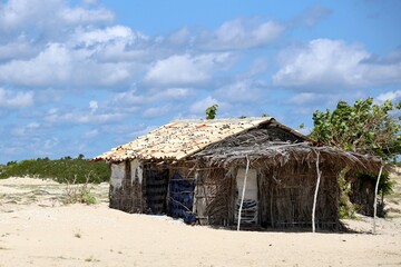 Fototapeta na wymiar In the sand of the beach rustic house made of wattle and daub and adobe in northeastern Brazil. Poor housing used by fishermen near the sea.