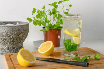 Moroccan mint in a pot, and in a glass, a sliced lemon and a black knife on a chopping board. Hot water in the glass. Cleanse, and a healthy lifestyle. Lemon slices being dropped in the glass