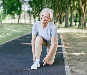 Portrait of a happy active beautiful senior woman posing fixing shoelace on her running shoe after...