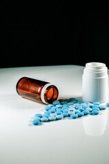 glass and White plastic pill's bottles with blue pills on white table. black background.  blue erection pills
