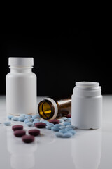 two plastic bottles and one glass with colored pills on a white table with a black background. various dietary supplements