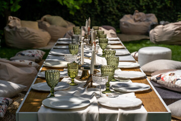 A set table in the garden, for special occasions. Empty plates and unusual glasses. Vintage tray, candleholder and vases with beautiful flowers.